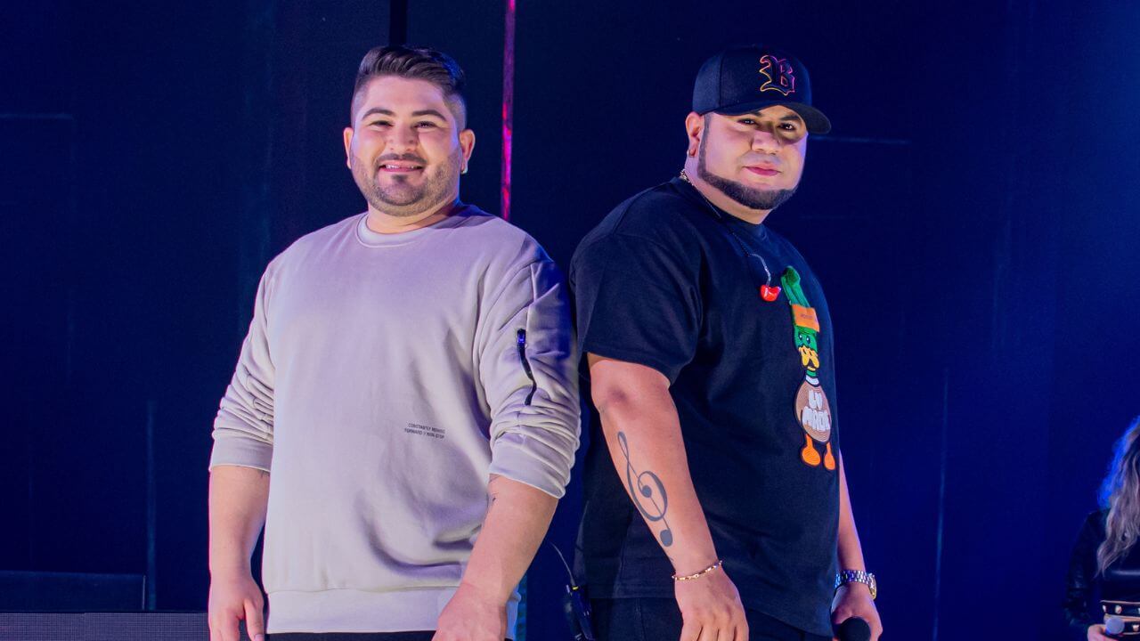 Dupla Os Barões da Pisadinha posando lado a lado em frente a um fundo azul